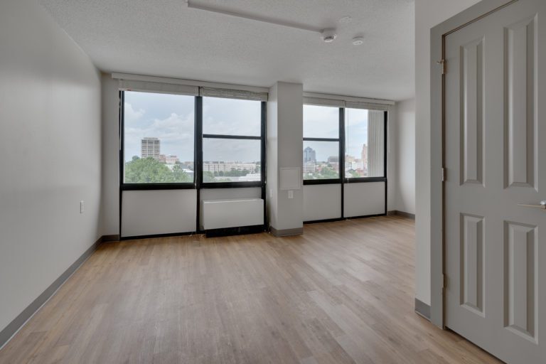 An empty bedroom with wooden floors and a wall of windows.