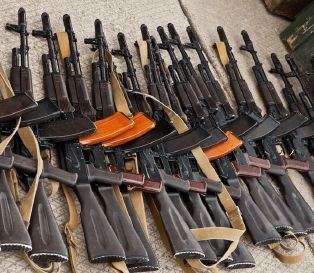 A row of assault riffles lined up on the ground.