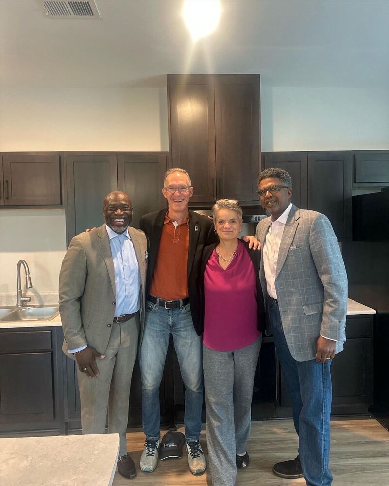 Four people stand and smile for a picture in the kitchen of the Vanguard Apartments.