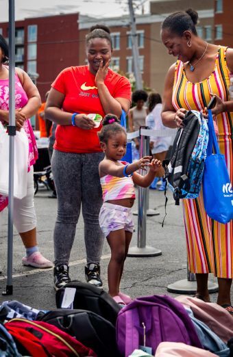 A little girl picking out a backpack while two women smile and watch.