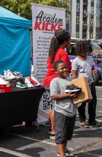 A little boy smiling while holding a box with new shoes.