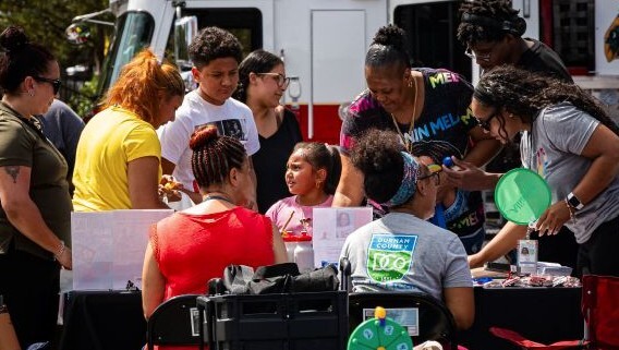 A group of individuals sitting and standing around a vendor booth.