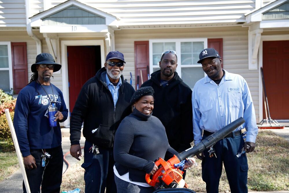 A woman holding a leaf blower, stands with four men for a picture.