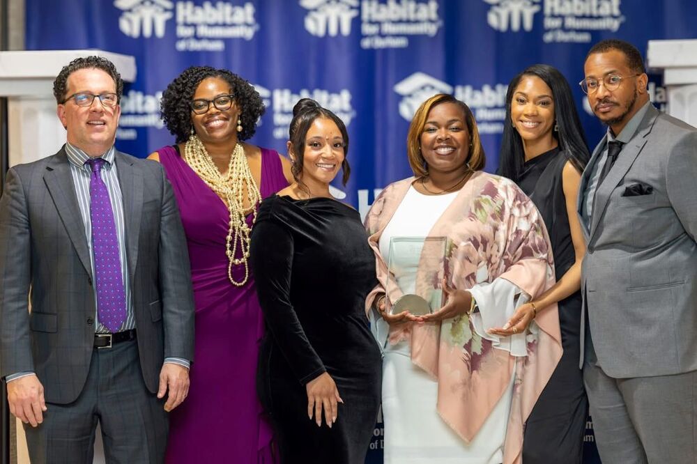 Six individuals talking a group photo while one of them hold the Community Partner Award.