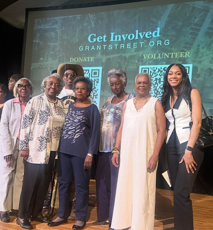 Seven individuals posing for a group photo with a backdrop that says Get Involved, Grantstreet.org. Donate. Volunteer.