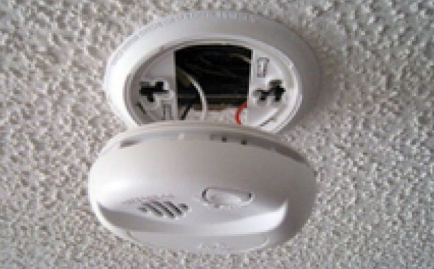 A close-up of a disconnected smoke detector hanging from the ceiling.