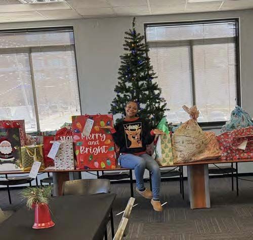 A woman sitting on a table that is full of wrapped Christmas gifts.