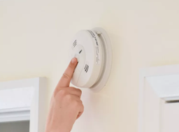 An individual pressing the button on a smoke detector to test it.