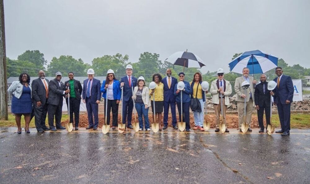 16 adults (men and women) standing with shovels, hard hats and umbrellas for the groundbreaking