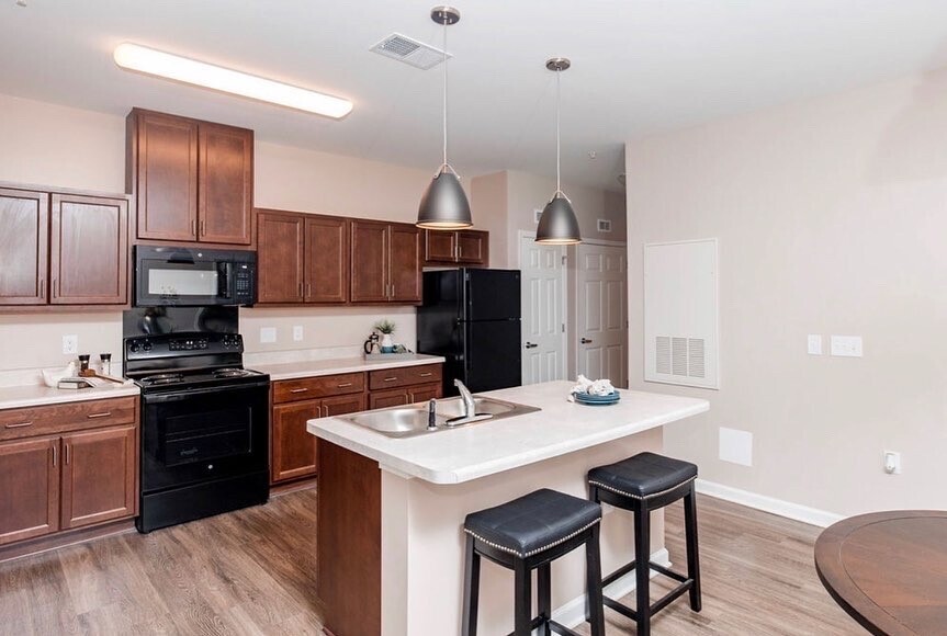 An empty apartment kitchen with a stove, cabinets and a sink with barstools.