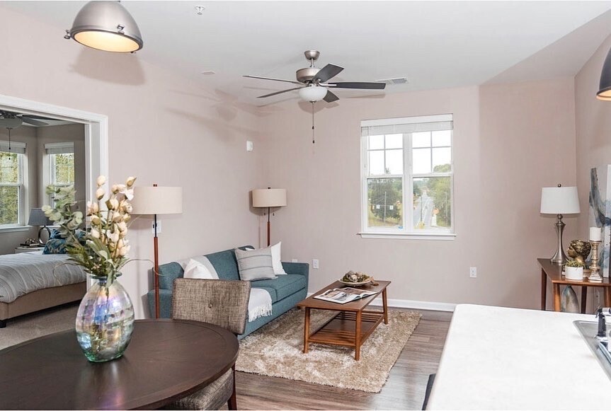 An apartment living room with a couch, two lamps, a rug and three tables.