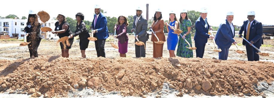 Twelve individuals with shovels in a line while throwing dirt into a pile at the Commerce Ground Breaking Ceremony.