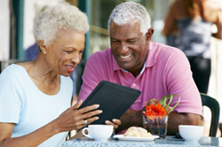 A couples sits at a table outside, looking at an iPad together,