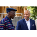 Two gentlemen stand together smiling and talking. 