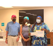 Three individuals standing next to one another, one individual is holding flowers and a scholarship award.