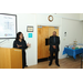 A woman speaking at a podium while a man stands in close proximity of her. 