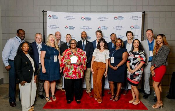 DUHANCAwardGroupPhoto.jpg A big group of individuals posing with an award in front of a North Carolina Housing backdrop.