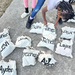 Several white drawstring back packs labeled with various individuals names.
