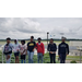 Seven students stand outside an airport while a plane takes off in the background.