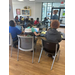 A group of people sitting at tables, on computers, listening to an instructor.