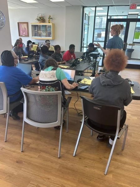 Kamdencomputerclass.jpg A group of people sitting at tables, on computers, listening to an instructor.