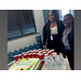  Two women smiling big while standing behind a cake and refreshments. 