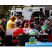  A group of individuals sitting and standing around a vendor booth. 