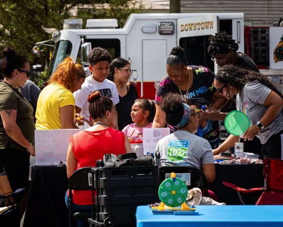 A group of individuals sitting and standing around a vendor booth.