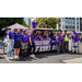  A group of individuals wearing purple while siting and standing around a purple car. 