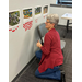  A woman kneeling on the ground to look at photos on the wall and trying to figure out where to put a red dot. 